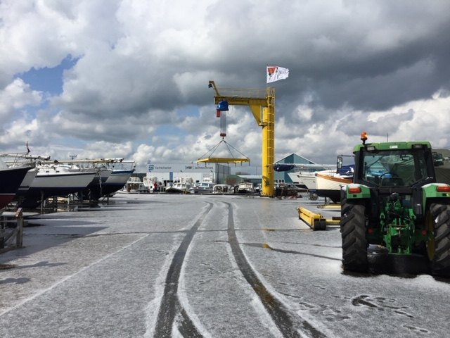 Het terrein in de sneeuw met boten op bokken, de gele kraan en een groene tractor